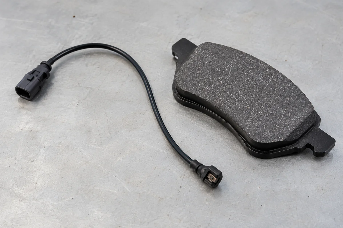 A brake wear sensor lead beside a new brake pad