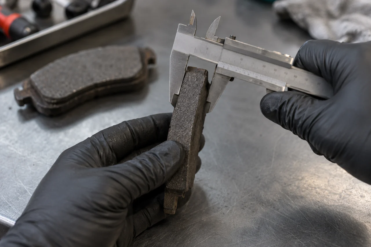 Technician measuring the friction material on a removed brake pad