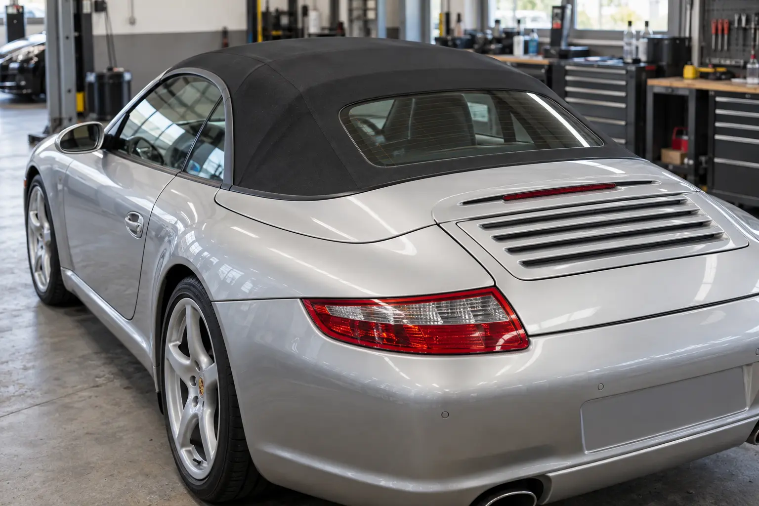 Silver Porsche 911 Cabriolet with a closed black fabric roof in a workshop